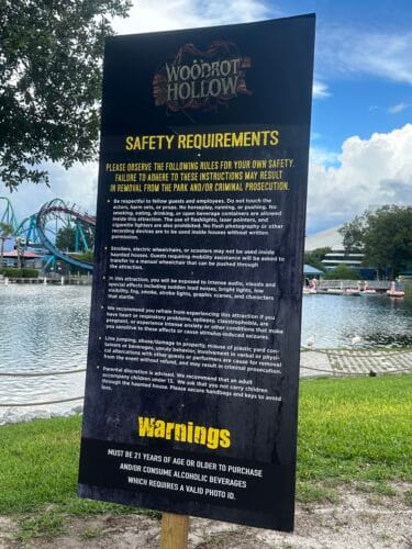 Woodrot Hollow safety requirements sign beside water and roller coaster track