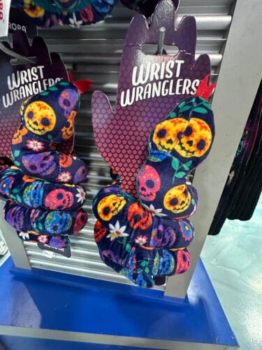 Coiled navy Wrist Wranglers plush snakes patterned with colorful sugar skulls, flowers, and green leaves.