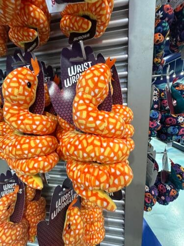 Orange coiled Wrist Wranglers plush snakes covered in yellow and white candy corn shapes.