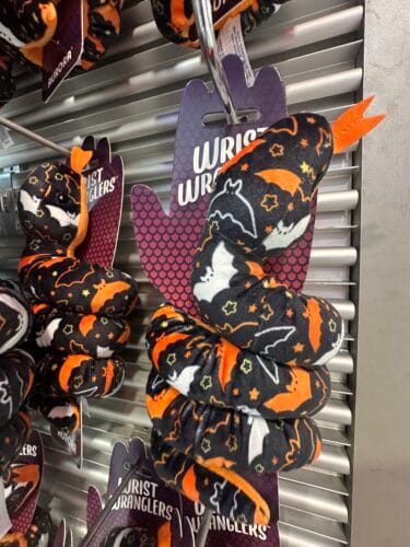 Black coiled Wrist Wranglers plush snakes patterned with orange and white bats and small stars.