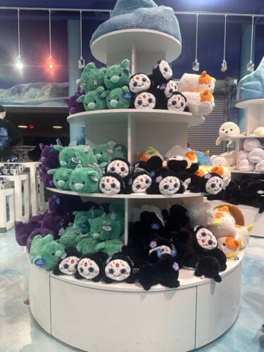 Round shelves filled with green monster plush, black plush with floral skull faces, and white plush with orange accents.